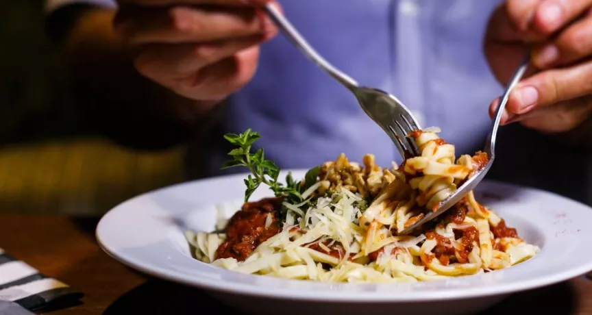 Personne dégustant une assiette de pâtes à la sauce tomate et au fromage dans un restaurant.