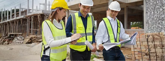 Une femme et 2 hommes en tenues de chantier sur un terrain de construction
