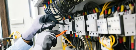 Mains équipées de gants travaillant dans une installation électrique 