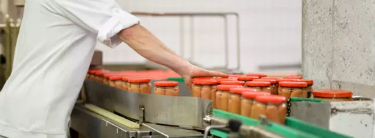 Homme travaillant dans une usine alimentaire aidant à la mise en pot de bocaux de saucisses
